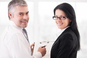 Business people doing paperwork. Two smiling business people writing something in note pad and looking over shoulder photo