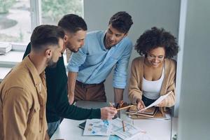 equipo de negocios joven confiado que tiene una reunión rápida mientras está de pie en la oficina juntos foto