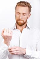 Everything should be perfect. Confident young bearded man adjusting sleeves while standing against white background photo