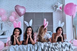 sentirse inseguro. cuatro hermosas mujeres jóvenes con orejas de conejo mirando hacia otro lado mientras están acostadas en la cama foto