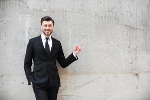 Pointing a copy space. Thoughtful young man in formalwear pointing away while standing outdoors photo