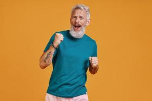 Senior man making a face while standing against orange background photo