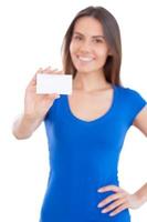 copie el espacio en su mano. Atractiva mujer sonriente joven que muestra una tarjeta de visita y sonriendo mientras está de pie aislado en blanco foto