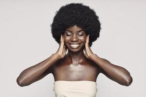 retrato de una hermosa joven africana que cubre las orejas con las manos mientras se enfrenta a un fondo gris foto