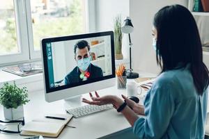 Serious young woman in protective face mask talking to collegue by video call photo
