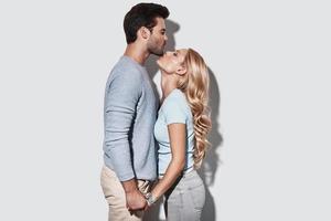 Loving everything about her. Beautiful young couple holding hands and kissing while standing against grey background photo