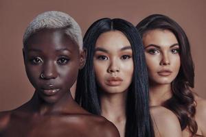 Young and beautiful. Three attractive young women looking at camera while standing against brown background photo