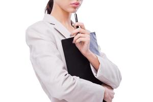 Thoughtful businesswoman. Close-up of confident young businesswoman holding clipboard and pen on chin while standing against white background photo
