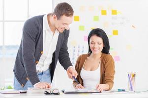 Working on the project together. Beautiful woman working together with cheerful young man pointing on notes and smiling photo