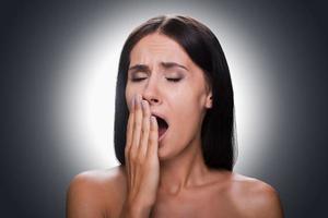 Feeling sleepy. Portrait of bored young shirtless woman covering mouth by hand and yawning while standing against grey background photo