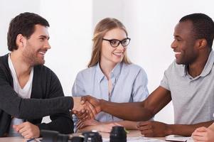 Friendly handshake. Two business people in casual wear handshaking while woman sitting between them and smiling photo