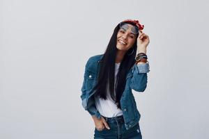 Attractive young woman in bandana adjusting eyewear and smiling while standing against grey background photo