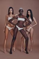 Born to be beautiful. Full length of three attractive mixed race women looking at camera while standing against brown background photo