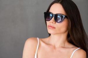 Confident in her perfect look. Attractive young woman in sunglasses looking away while standing against grey background photo