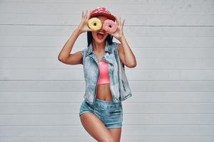 She do not know what the boredomis. Playful young women holding donuts against her eyes and smiling while standing against the garage door photo