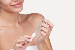 Nail care. Cropped image of smiling young woman wrapped in towel polishing her nails and smiling while standing against grey background photo