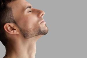 hombre guapo con barba. vista lateral de un apuesto joven barbudo que mantiene los ojos cerrados mientras se encuentra aislado en un fondo gris foto