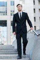 Successful businessman. Full length of cheerful young men in formalwear holding briefcase while walking outdoors photo