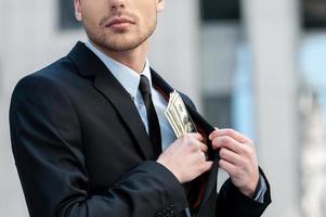 Pocketing company money. Cropped shot of a businessman placing money into his pocket photo