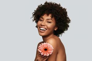 Dangerously beautiful. Attractive young African woman looking at camera and holding a flower while standing against grey background photo