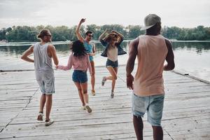 totalmente feliz grupo de jóvenes con ropa informal sonriendo y gesticulando mientras disfrutan de la fiesta en la playa foto