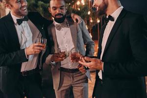 Three well-dressed men drinking whiskey and communicating while spending time on party photo