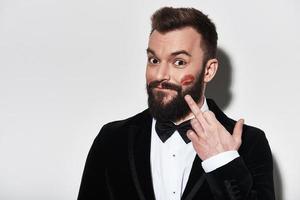 Ladies love him Handsome young man in full suit pointing at lipstick marks and smiling while standing against grey background photo