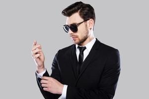 Used to perfection. Handsome young man in formalwear adjusting his sleeve while standing against grey background photo