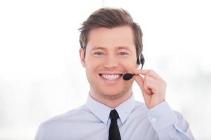 alegre representante de servicio al cliente. apuesto joven con camisa y corbata ajustando sus auriculares y sonriendo a la cámara foto