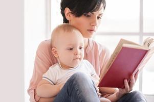 leyendo un libro juntos. joven madre sosteniendo al bebé y leyendo un libro foto