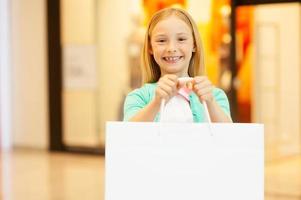 Copy space on her shopping bag. Cheerful little girl holding shopping bag and smiling while standing in shopping mall photo