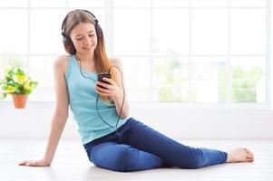 escuchando la música en casa. linda adolescente con auriculares escuchando música mientras se acuesta en el suelo en su apartamento foto