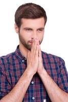 Generating fresh ideas. Portrait of thoughtful young man in casual shirt holding hand on chin and looking at camera while standing isolated on white photo