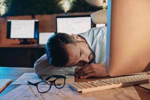 Exhausted young man sleeping at his working place while staying late in the office photo