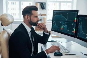 Concentrated young man in shirt and tie analyzing data on the stock market while working in the office photo