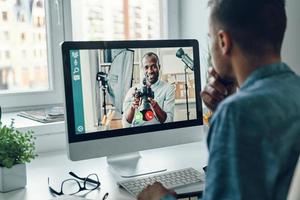 Confident young man talking to collegue by video call while sitting in office photo