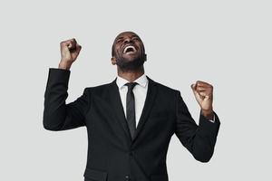 Happy young African man in formalwear cheering while standing against grey background photo