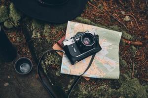 cosas que necesitas en el bosque. cerrar la vista superior de la cámara digital, el mapa, el sombrero y el recipiente aislado para bebidas en el suelo del bosque foto