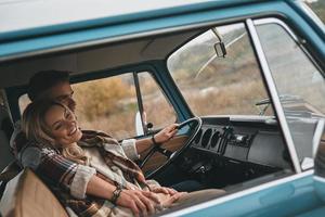 Totally happy. Beautiful young couple embracing and smiling while sitting in blue retro style mini van photo