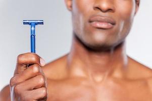 Man holding razor blade. Cropped image of young shirtless African man holding razor blade while standing isolated on grey background photo