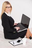 ocupado y confiado. vista superior de una mujer de negocios madura y confiada mirando por encima del hombro y sonriendo mientras se sienta en la escalera y trabaja en una laptop foto