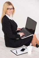 Busy and confident. Top view of confident mature businesswoman looking over shoulder and smiling while sitting at the staircase and working on laptop photo