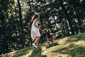 disfrutando del tiempo sin preocupaciones. toda la longitud de una linda niña jugando con su perro mientras corre al aire libre foto