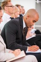 Making some urgent notes. Side view of business people writing something in their note pads while sitting in a row photo