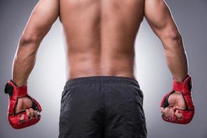 Ready to fight. Rear view of shirtless African man in boxing gloves standing against grey background photo
