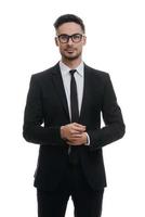 Portrait of style. Handsome young man in full suit adjusting his sleeve and looking at camera with smile while standing against white background photo