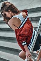 Making sport wear look sexy. Rear view of beautiful young woman in sport clothing keeping eyes closed while leaning on the railing outdoors photo