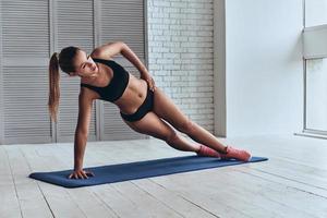 segura de su régimen de fitness. hermosa mujer joven en ropa deportiva manteniendo la pose de tablón lateral mientras hace ejercicio en el gimnasio foto