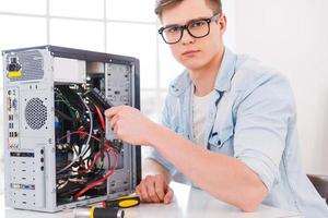 maestro de computadoras. retrato de un joven apuesto que repara una computadora mientras está sentado en su lugar de trabajo foto