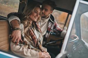 simplemente enamorado. hermosa pareja joven abrazándose y sonriendo mientras se sienta en una mini furgoneta de estilo retro foto